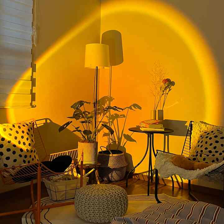 温かみのあるオレンジ色の照明が灯るリビング、フロアランプとモンステラの植物、クッションとサイドテーブルが配置された居心地の良い空間