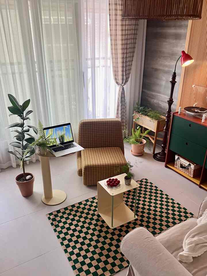 黄色のチェック柄アームチェアとグリーンのチェッカー柄ラグ、観葉植物、明るいカーテンが配置された温かみのある自然な雰囲気のリビング