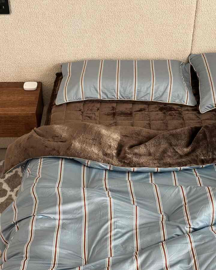 ブラウンとブルーの色調の寝室、ベッドと枕、ナイトテーブルが配置された落ち着いた空間