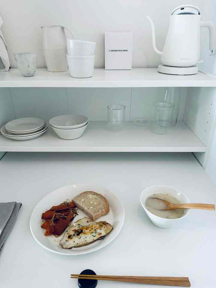 モノトーンの白いキッチン、整然と並んだ皿と電気ケトルが配置されたミニマルな雰囲気のインテリア