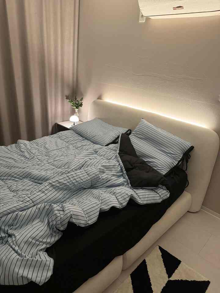 White and blue toned bedroom featuring LED-backlit headboard, cozy bedding, and blackout curtains creating a warm atmosphere