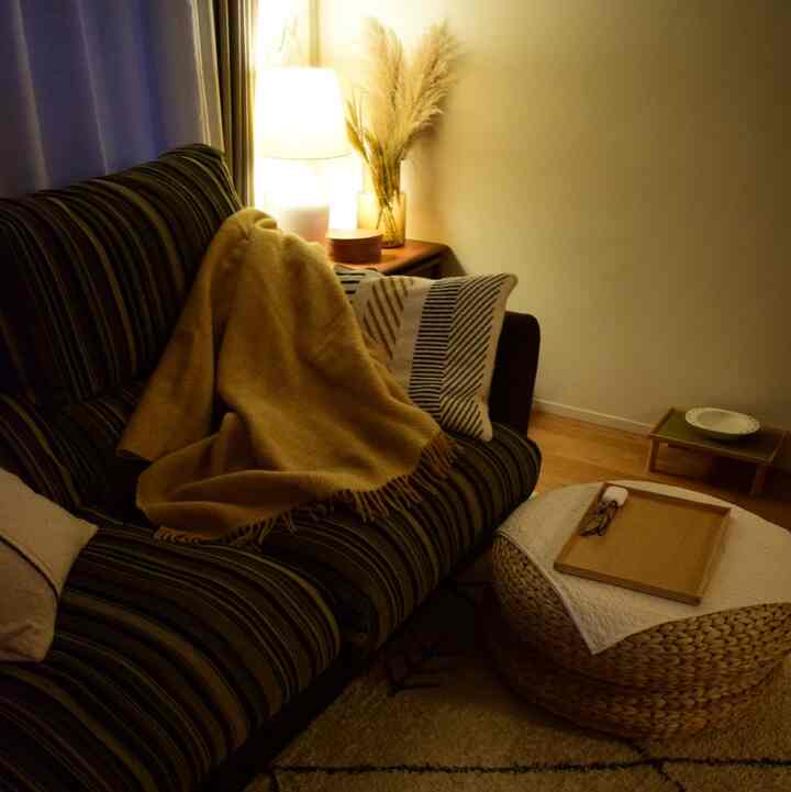 Warm ochre wood-toned vintage living room featuring a striped sofa with yellow throw and a woven pouf creating cozy atmosphere