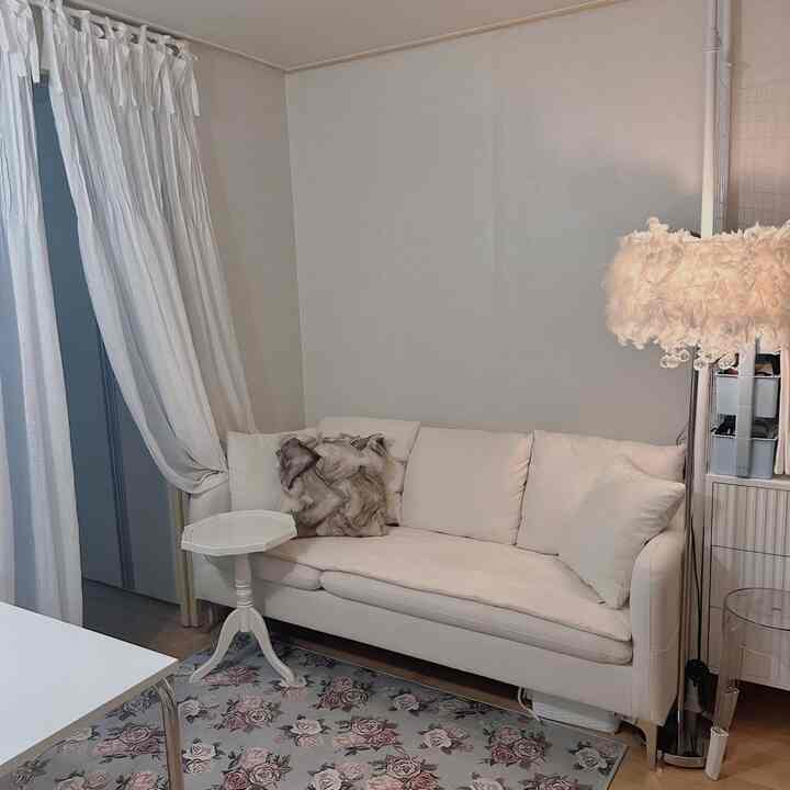 白を基調としたワンルームのリビング、白のソファとフロアランプ、花柄のラグが配置された雰囲気のある空間