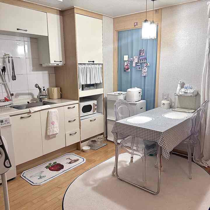 ホワイトと木目調が調和した狭いキッチン、透明な椅子とギンガムチェックのテーブルクロスが配置された雰囲気のある空間