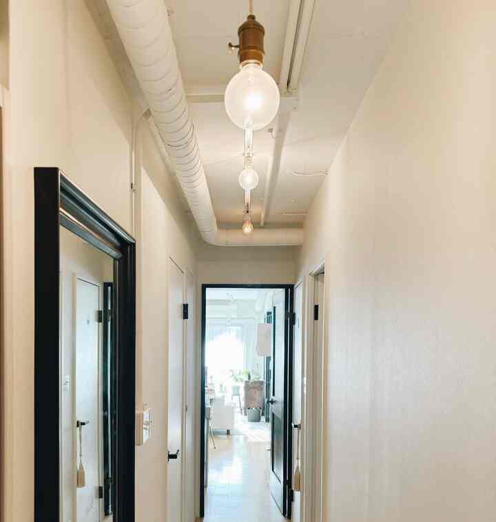 白い壁と天井、黒枠の鏡やドアが配置されたモダンな玄関の廊下