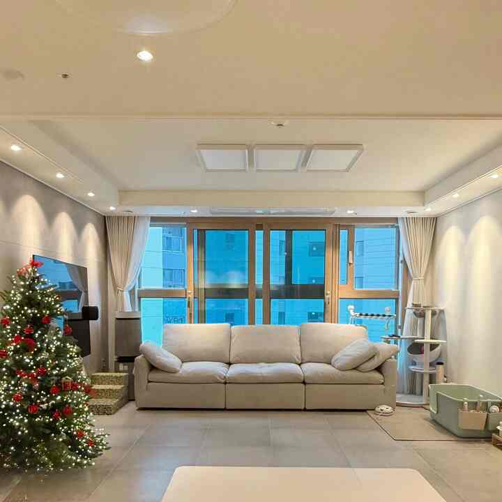 ベージュと白を基調としたリビング、中央に大きなソファと左側に飾られたクリスマスツリーが配置された温かみのある空間