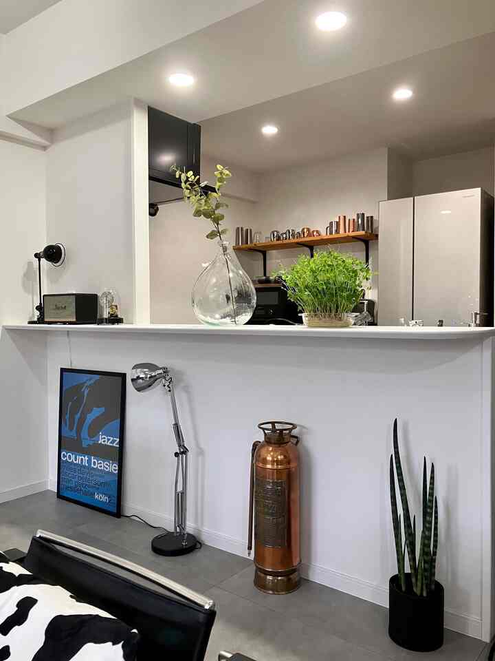 白を基調としたリビングとキッチンが繋がる空間、ヴィンテージの消火器と緑の植物がインダストリアルな雰囲気を醸し出すモダンなインテリア