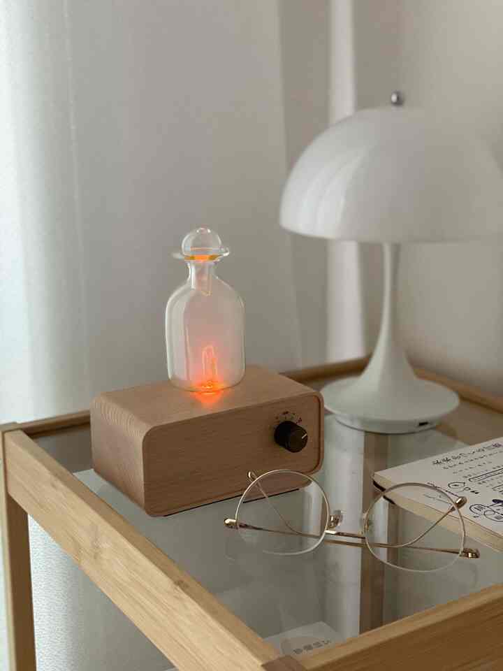 ナチュラルな色調の寝室のサイドテーブルにアロマディフューザーと白いテーブルランプが配置された雰囲気のある空間