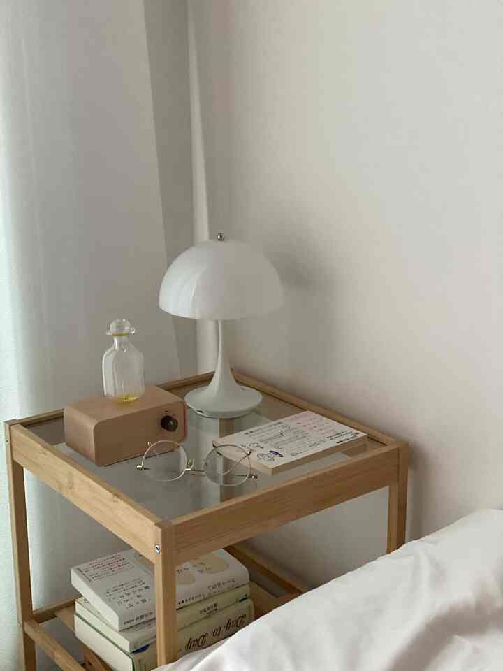 白と木目調の寝室のナイトテーブル、テーブルランプ、本、アロマディフューザーが配された雰囲気のあるインテリア