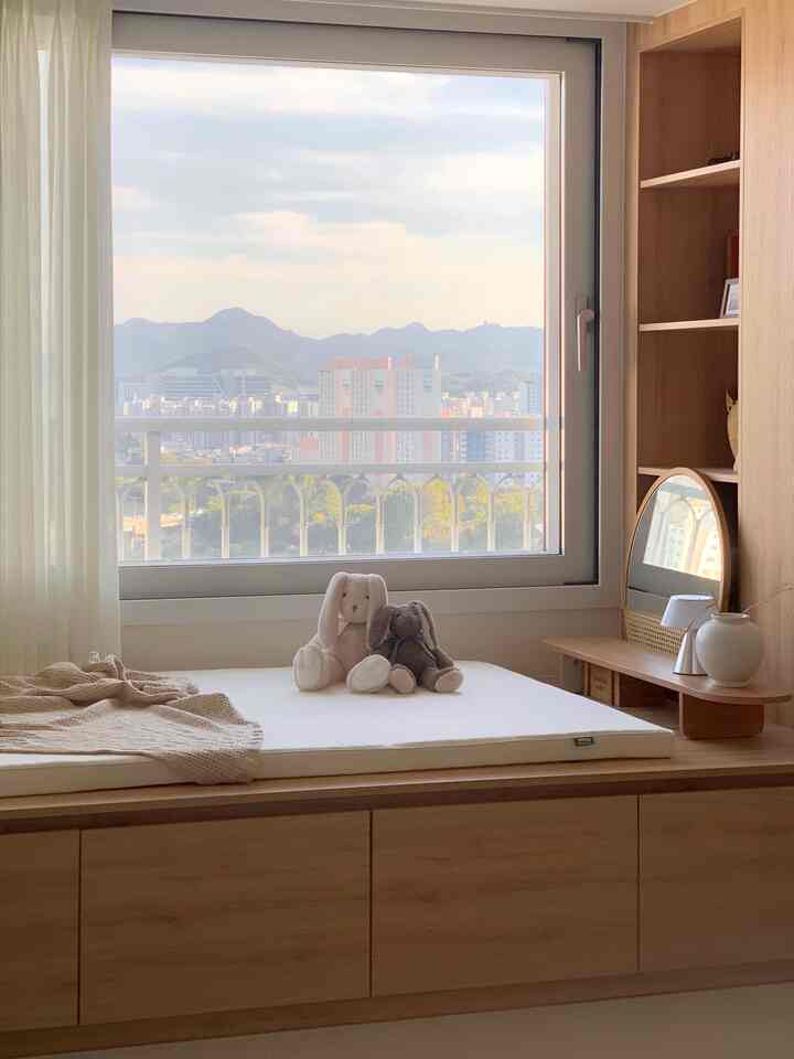 ベージュとホワイトの色調のリビングスペース、木製の平床型ベッドとマットレス、ぬいぐるみが置かれた温かみのある昼寝空間