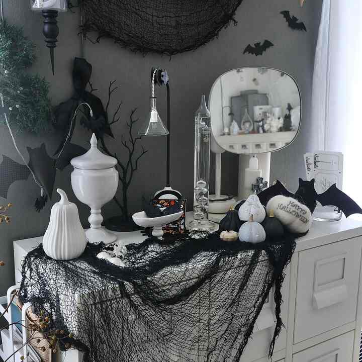 モノトーンのリビング空間、白い家具の上に黒いクモの巣の装飾とハロウィンのオーナメントが配置されている
