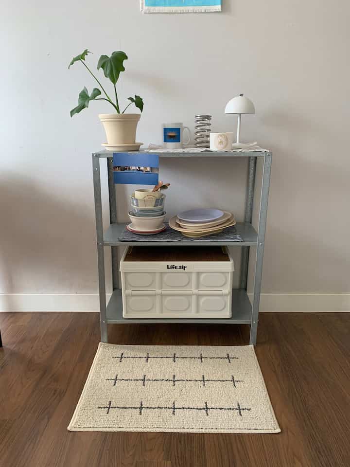 ベージュの壁とナチュラルな木の床の空間、金属製の棚に植物と食器が配置されたシンプルな室内