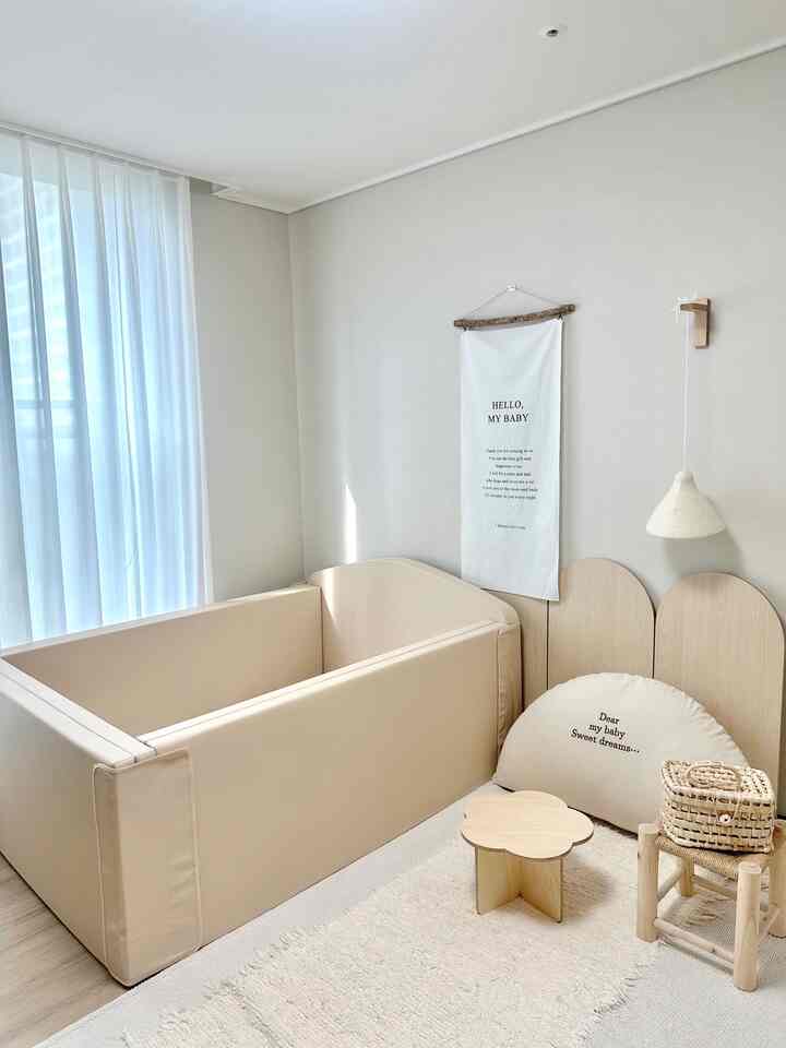 ベージュトーンの子供部屋、ベビー用ベッドとナチュラルな木製家具、居心地の良いラグが配置された雰囲気のあるインテリア