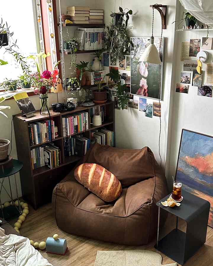 自然なウッドトーンの小さな部屋、ブラウンのビーズクッションと本棚、多くの植物が配置された居心地の良い空間