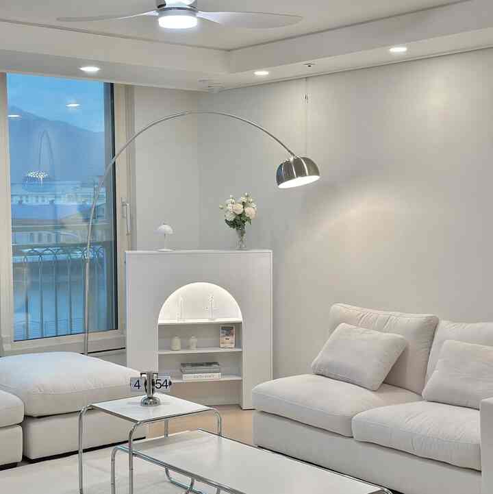 White and silver toned living room featuring spacious sofa, steel table, and Arco steel floor lamp in a simple modern setting