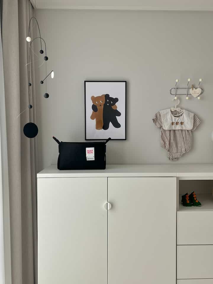 白い壁とイケアプラッツァのクローゼットが配置されたベビールーム、ポスター額とモビールがシンプルに飾られた空間