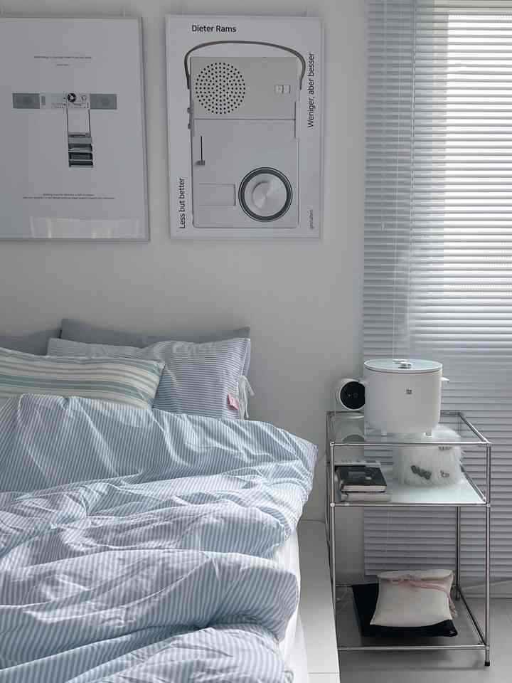 白とライトブルー調の寝室、ミッドセンチュリーポスターときちんとしたベッドが配置された、清潔で落ち着いた雰囲気のインテリア