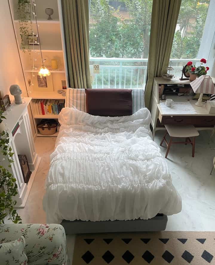 白とオリーブグリーンの色調の寝室、中央にベッドとデスク、遮光カーテン、ヴィンテージ風の小物が配置された雰囲気のあるインテリア