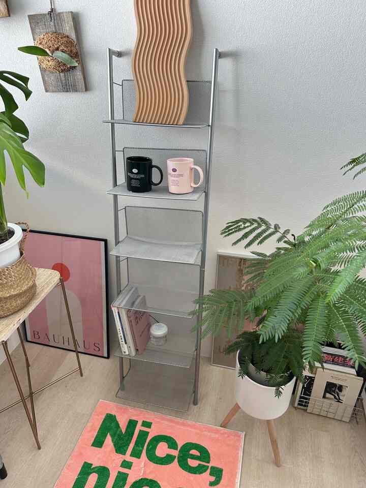 White walls and natural tone floor feature a shelving storage unit with plants and decorative objets creating a harmonious space