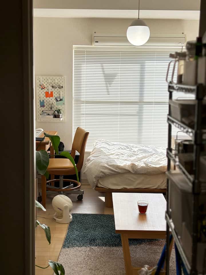 White and brown toned single household 7-tatami room with desk, chair, bed, and open shelf in a natural, compact space