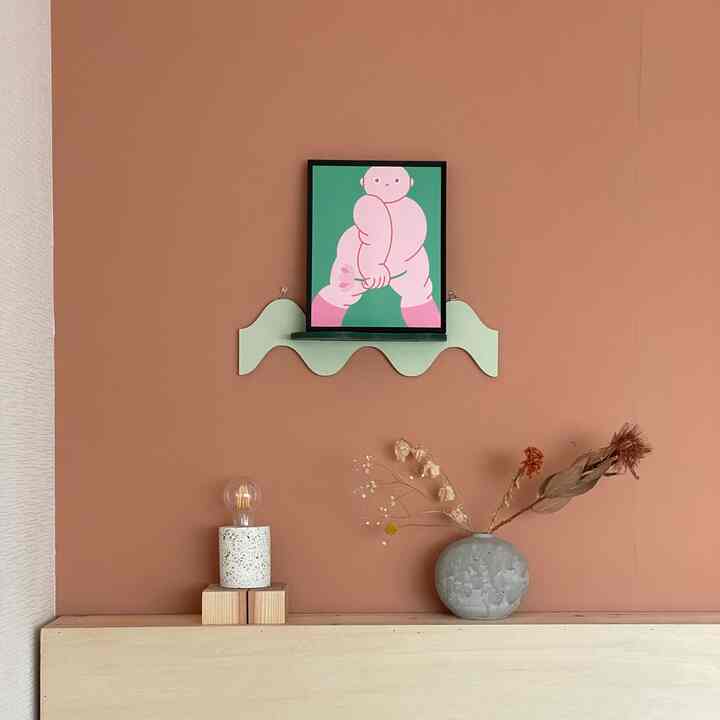 テラコッタ色の壁にアールデコ風の波型シェルフとピンクと緑のポスターが配置された落ち着いた雰囲気のインテリア