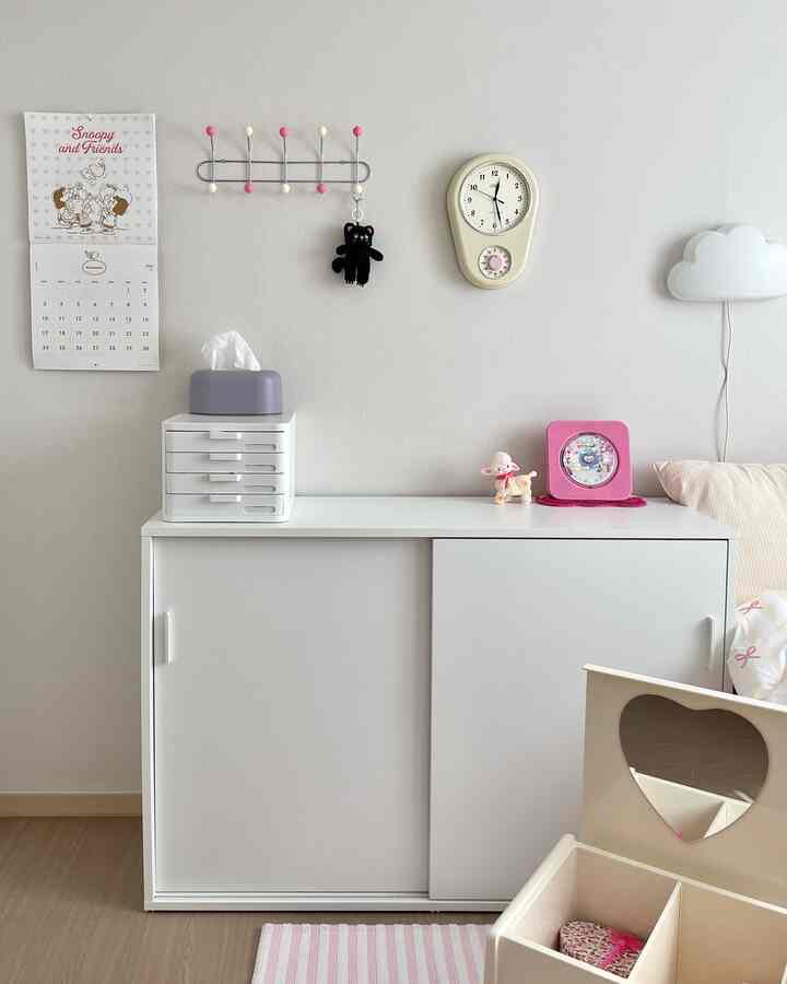 白とピンクのトーンが調和した子供部屋、すっきりとしたキャビネットとおもちゃ収納が配置されたミニマルな空間