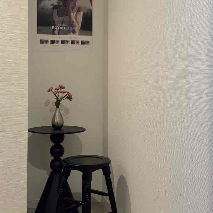 ベージュ色の壁と黒いスツール、サイドテーブル、花瓶が配置されたシンプルなコーナーの印象的な空間