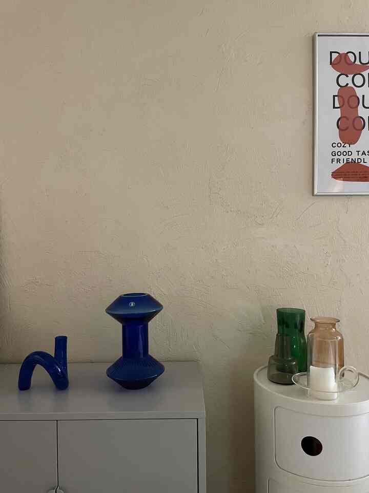 ホワイトの壁と家具の上にブルーとグリーンの花瓶、ミッドセンチュリーモダンの雰囲気を持つ1LDKリビングの一角にポスターが配置された空間