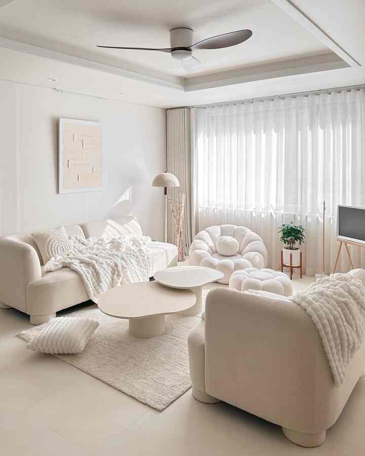 柔らかいナチュラルカラーのリビング、ブークレソファとひざ掛け、カーテンが配置された温かみのある空間