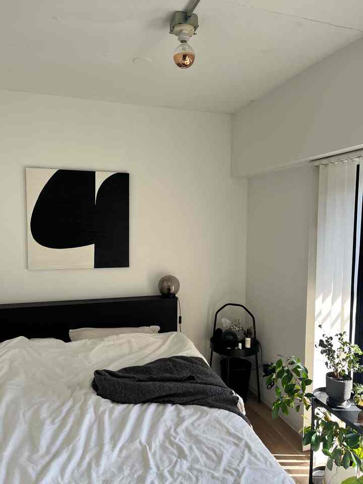 白と黒を基調としたナチュラルモダンな寝室、白いベッドと黒いナイトテーブル、壁に抽象画が配置された落ち着いた空間