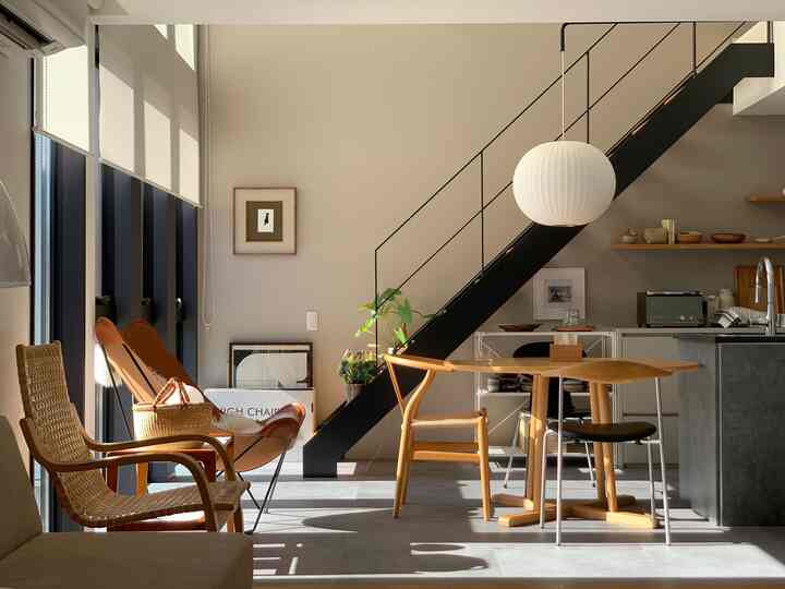 Soft wood-toned Mid-Century Modern dining room featuring black staircase and white pendant lighting