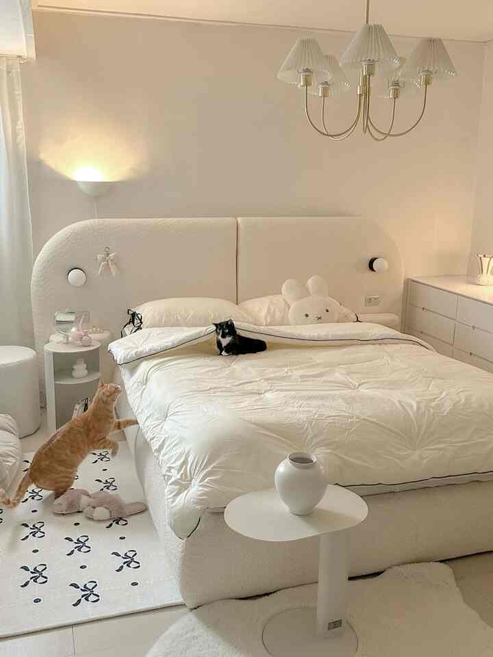 White-toned bedroom featuring a soft fabric bed and bedding, with two cats adding a cozy atmosphere