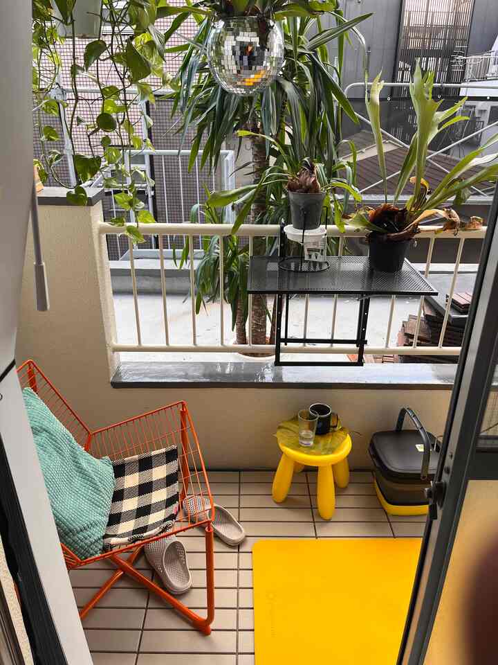 Bright yellow and orange-themed balcony featuring a children's stool, outdoor chair, and various plants creating a cozy outdoor space