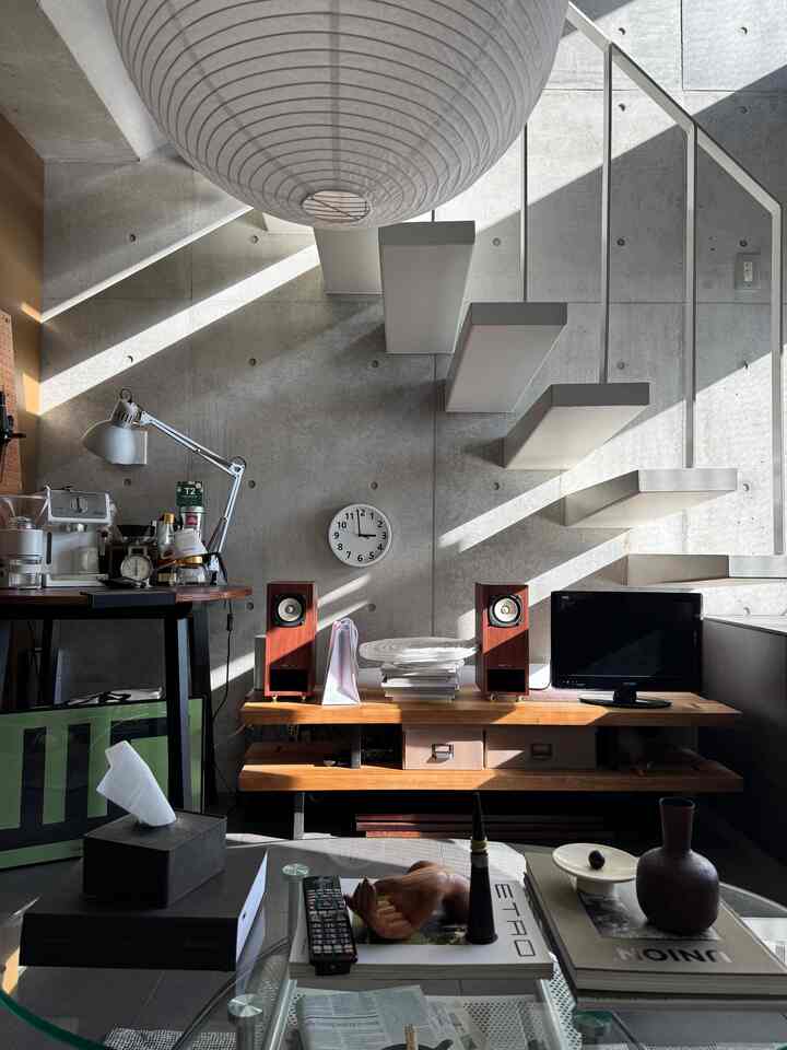 グレーのコンクリート壁と木目調家具が調和したモダンなリビング、中央にテレビ台とソファ、丸い天井照明が配置された印象的な空間