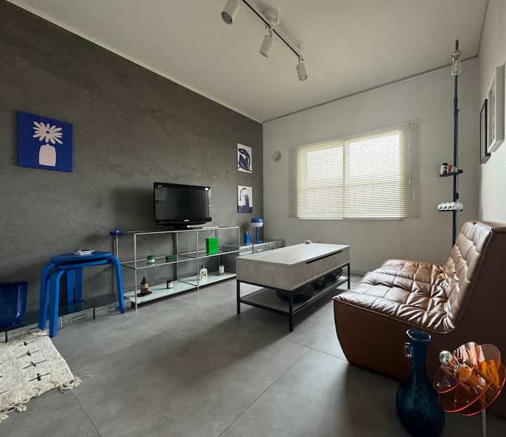 Blue and gray toned living room featuring a modern sofa, metal TV stand, and lighting near window
