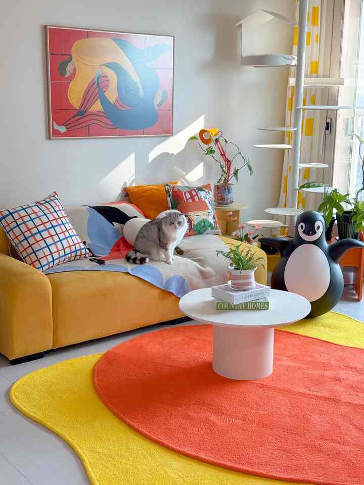 明るい黄色とオレンジの色調のリビング、ソファに座る猫と丸いコーヒーテーブル、ペットのおもちゃと植物が配置された雰囲気のある空間