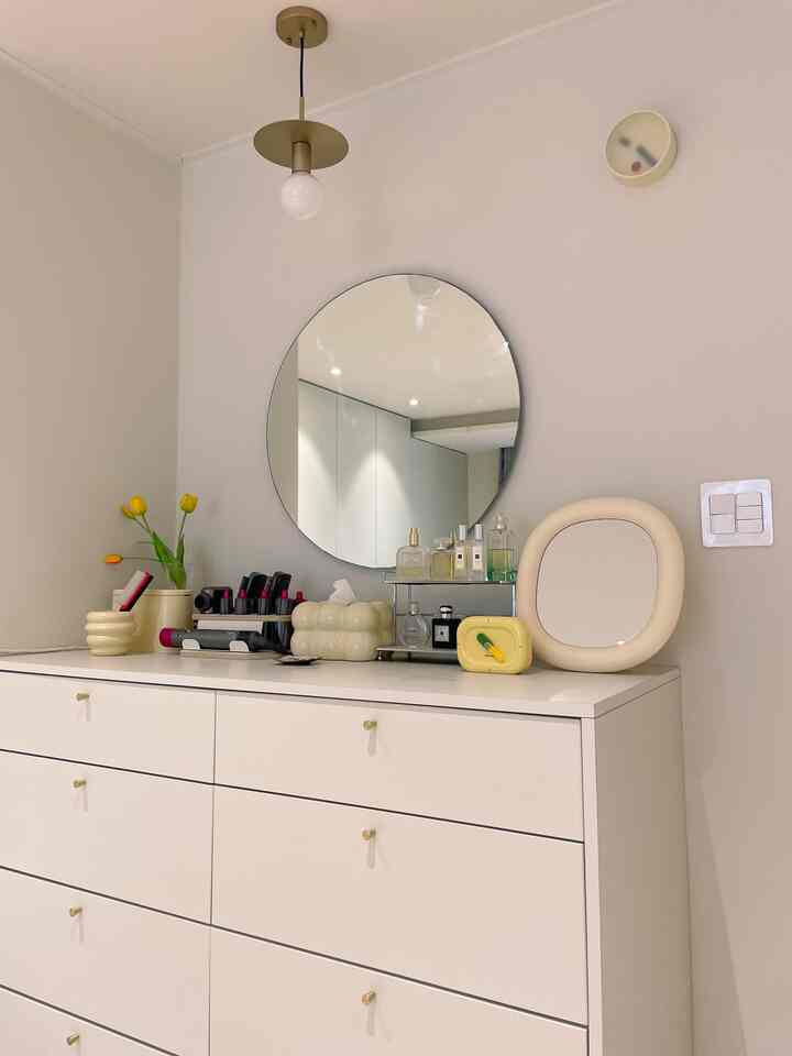 ホワイトとクリームベージュのトーンが調和したミニマルなパウダールーム、丸い鏡と収納棚が配置された印象的な空間