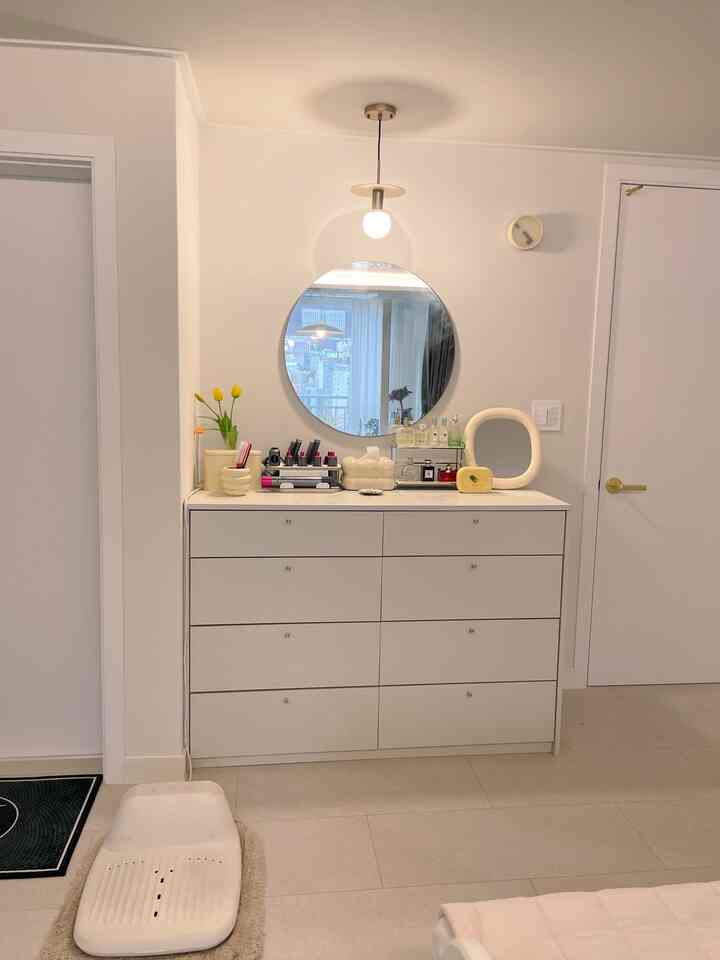 柔らかなホワイトトーンの寝室、中央に丸い鏡と化粧台が配置された清潔な印象的な空間