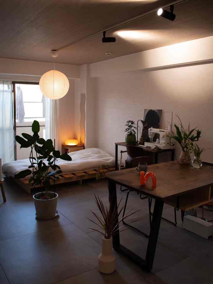 ナチュラルトーンと木目調が調和したワンルームの寝室兼ワークスペース、植物と照明が温かみのある雰囲気を演出