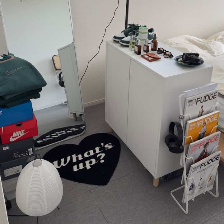 白とグレーのトーンのワンルーム、白い収納キャビネットと全身鏡、靴箱とマガジンラックが配置されたシンプルなインテリア