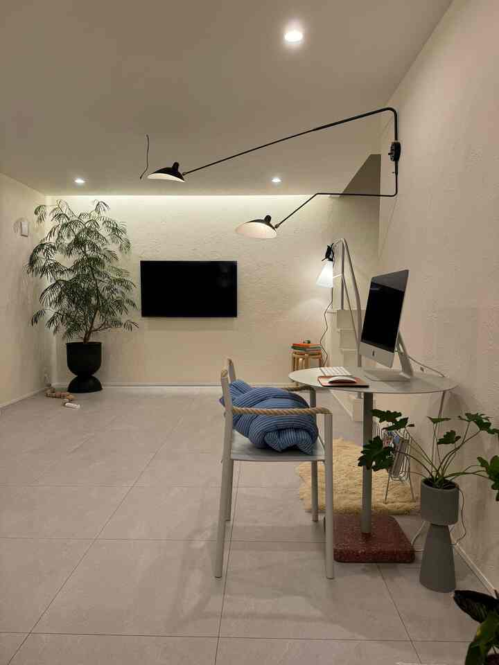 White and gray toned living room cum home office featuring wall-mounted TV and minimalist desk with a simple interior
