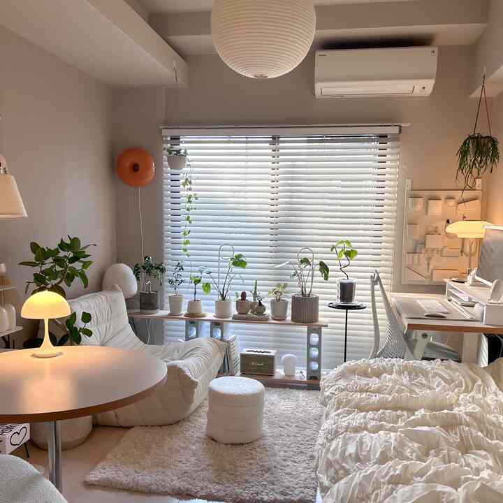 A predominantly white living and bedroom space featuring plants, a sofa, and a desk with a cozy and simple modern aesthetic