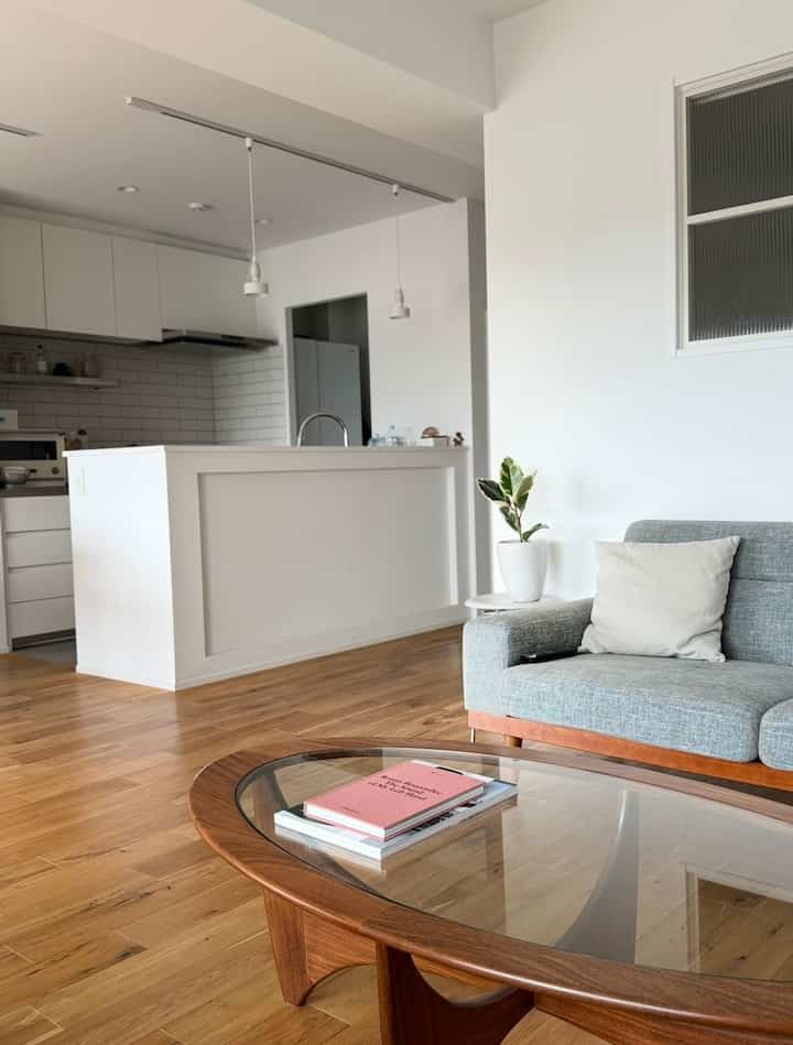 白と木目調の北欧リビング、グレーのソファとオーバル型のコーヒーテーブルが配置された清潔感のある自然な印象の空間