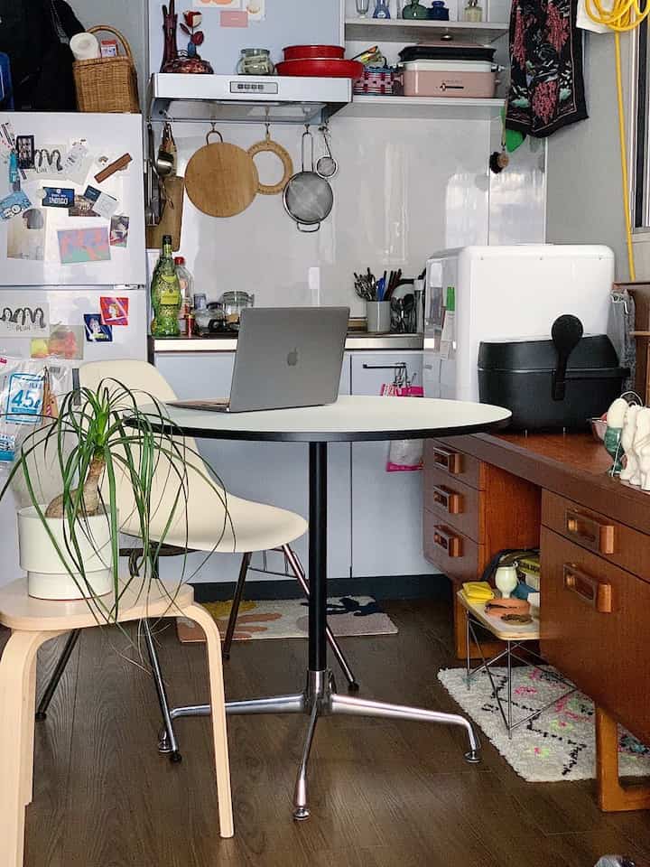 Natural color and wood tone compact kitchen space featuring a round dining table with laptop, creating a home office environment