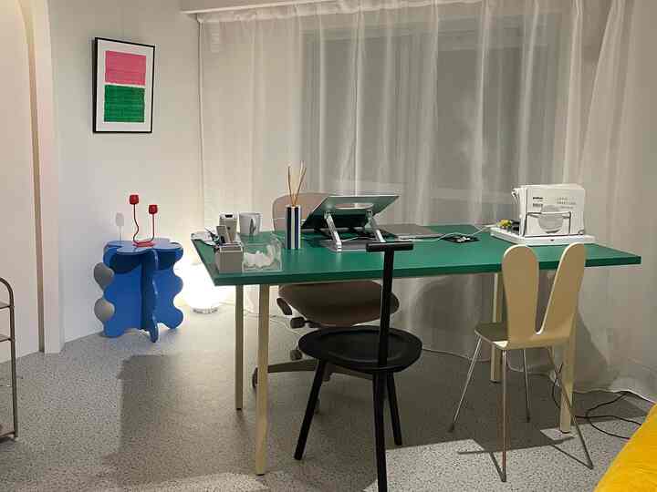 明るくモダンなホームオフィス、緑色の机とシンプルな椅子が配置され、透けるカーテンが背景にある空間