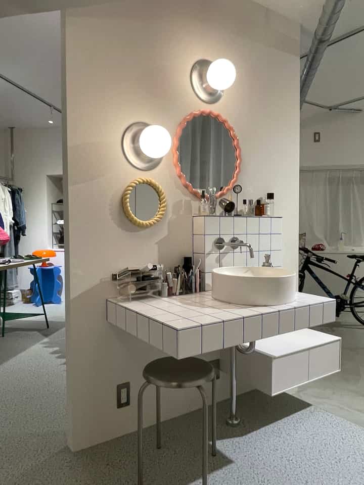 白とグレーのトーンのバスルーム、タイルの洗面台と個性的なフレームの丸い鏡が配置されたモダンな空間