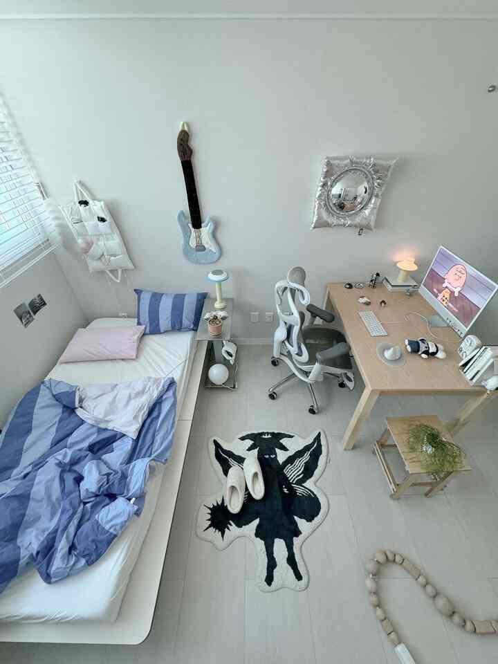 ホワイトとウッドトーンが調和した小さな一人暮らしの寝室、木製デスクとオフィスチェア、パステルブルーの寝具が配置されたモダンなインテリア