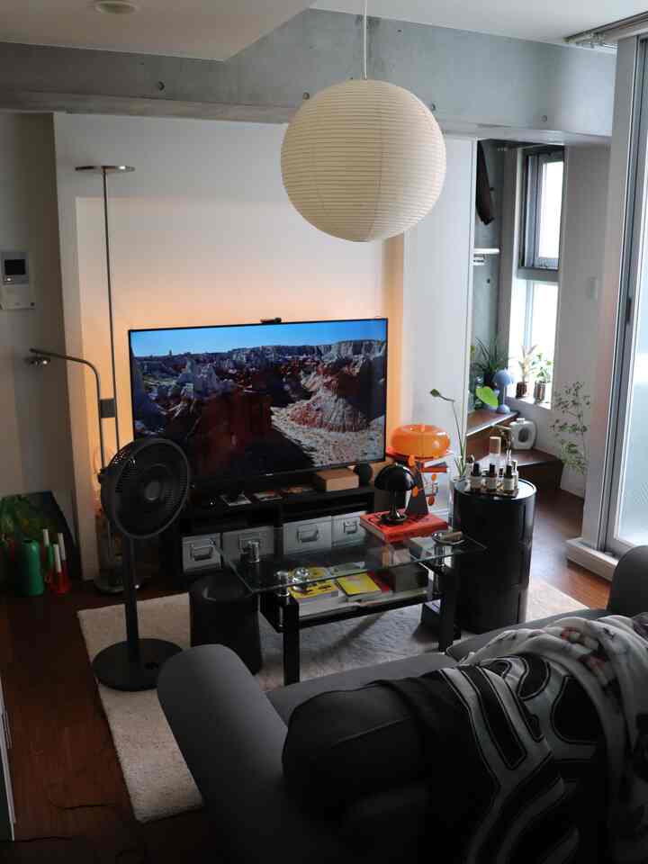 モノトーンとオレンジのアクセントが映えるミッドセンチュリーモダンのリビング、2人掛けのソファとテレビが配置された温かみのある空間