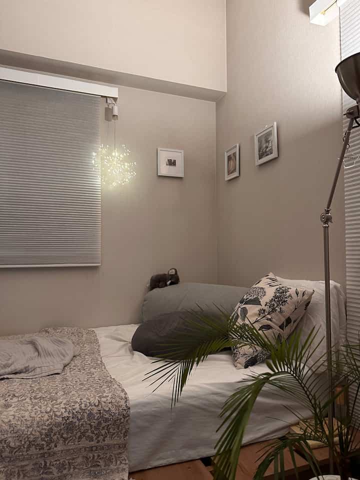 ベージュ調の寝室、中央にベッドと枕が配置され、左側にストリングライトがあり、温かみのある落ち着いたインテリア