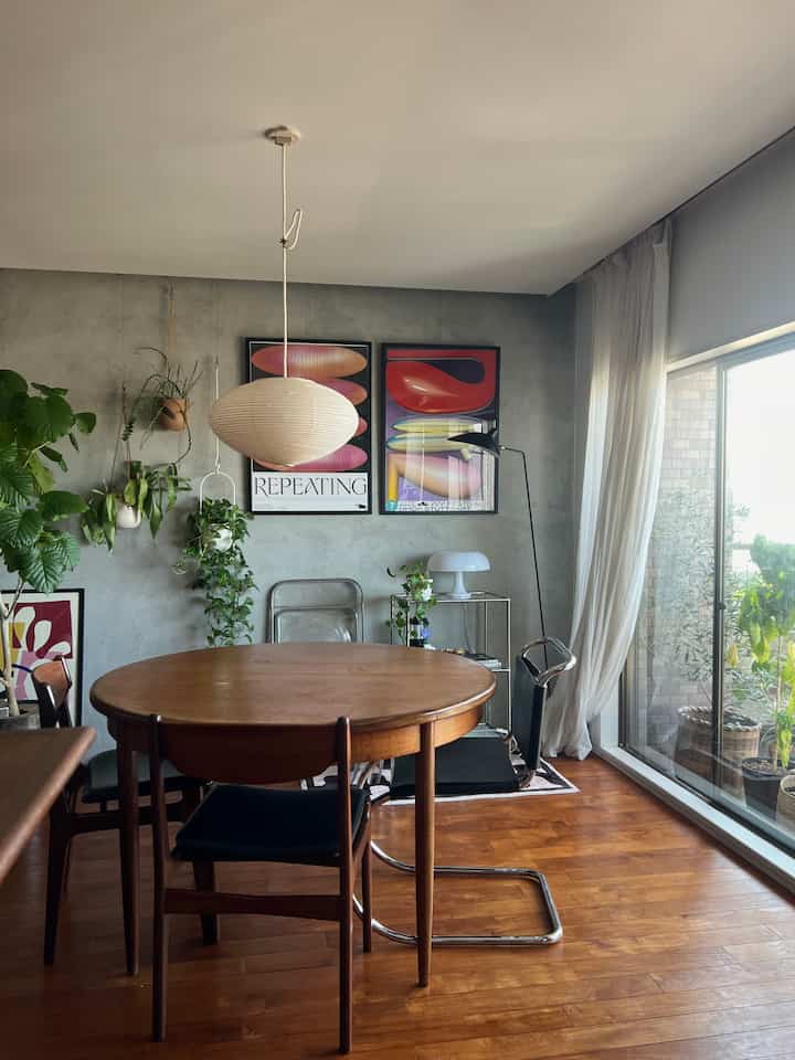 Natural wood-toned dining room with plants, bright balcony, and white pendant light creating a cozy atmosphere